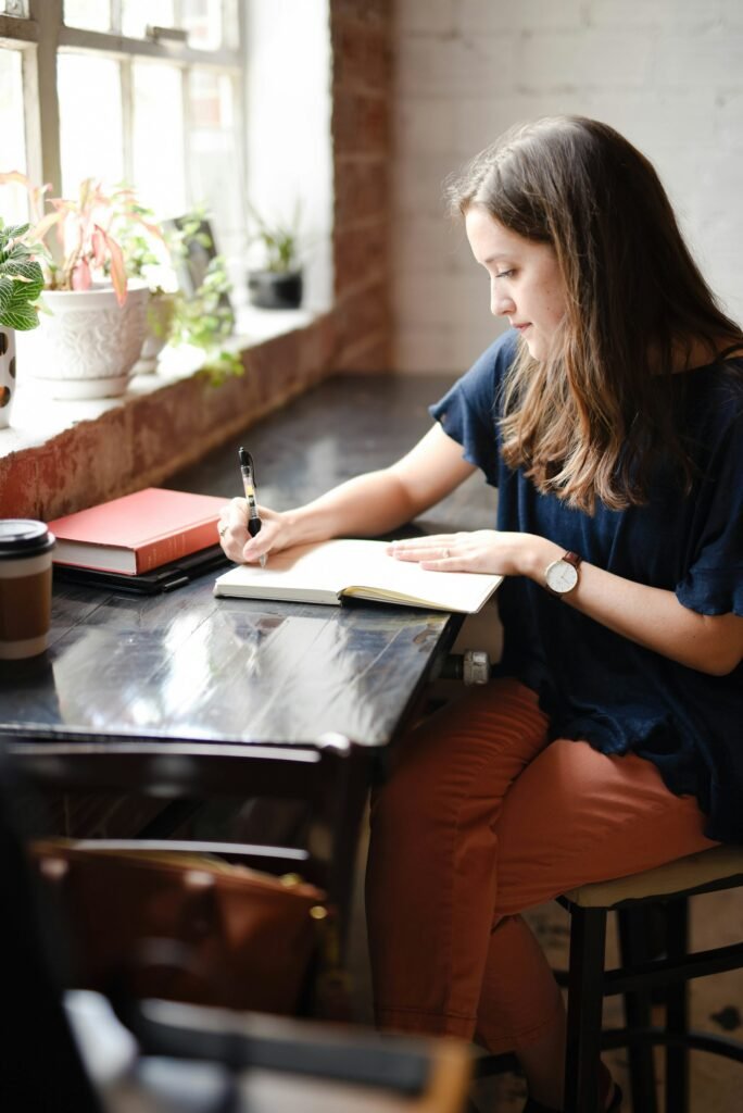 Vrouw schrijft in een notitieboek aan een tafel bij het raam